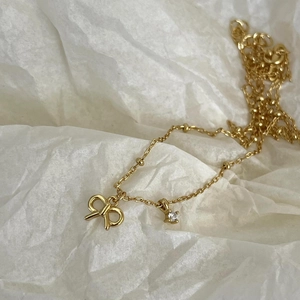 Detailed close-up of golden bow pendant and sparkling zircon on fine beaded chain necklace
