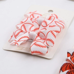 Detail view of baseball pattern bow hair clip made of white grosgrain ribbon with red stitching