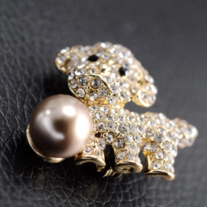 Close-up of golden dog brooch featuring sparkling rhinestones and a large champagne pearl