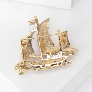 Elegant gold sailboat brooch with pearl accent and textured metal finish on white backdrop