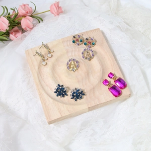 Close-up of assorted fashion earrings displayed on a wooden tray with lace and roses