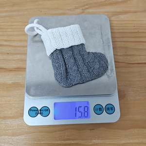 Detailed view of grey cable-knit mini Christmas stocking on scale weighing 15.8 grams