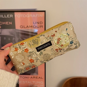 Close-up of floral embroidery texture and black logo patch on a beige fabric pouch