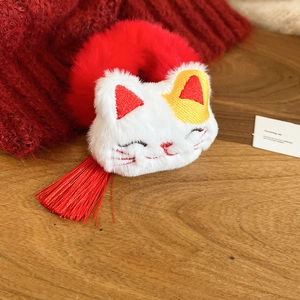 Close-up of plush Lucky Cat hair tie with white fur, red embroidery, and silk tassels