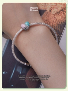 Detail of silver mesh bracelet featuring a pink and teal enamel heart charm with crown