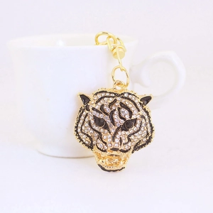 Golden tiger head keychain with sparkling rhinestones hanging on a white ceramic cup
