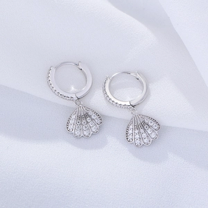 Close-up of silver shell drop earrings with pavé cubic zirconia on white fabric
