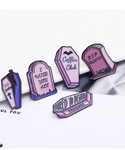 Detail of five gothic enamel pins with coffin and gravestone shapes in purple and pink