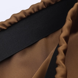 Close-up of premium brown satin skirt fabric with a black elastic waistband detail
