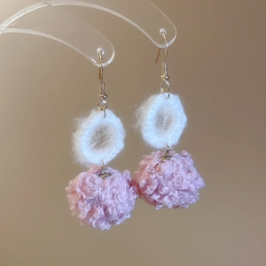 Dettaglio degli orecchini a uncinetto bianchi con pompon rosa pelosi per l'inverno