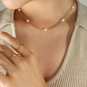 Golden flat chain necklace with freshwater pearls and gemstone rings on a model