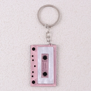 Close-up of pink and white tape cassette keychain with Friends text on beige texture