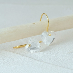 Detailed macro view of heart-shaped crystal drop earrings with golden hook on a white texture