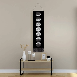 Black moon phase tapestry with fringe on beige wall above a wooden console table