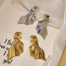 Detail shot of wavy pleated metal earrings in gold and silver finish with high luster