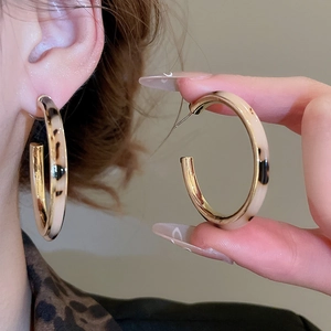 Detail view of large C-shaped leopard print resin hoop earrings with golden metal accents