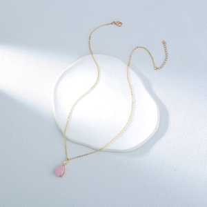 Detail of gold chain necklace with pink teardrop pendant on a white tray with side lighting