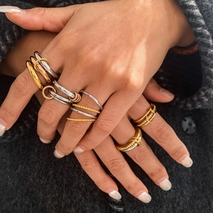 Detailed view of stacked 18K gold and silver rings with zircon accents on tweed fabric