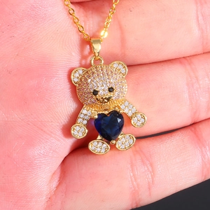Macro view of a gold bear pendant with white zircon and a blue heart held in hand