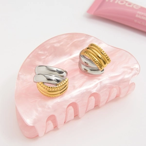 Two-tone 18K gold and silver twisted C-shape earrings on a pink marble background