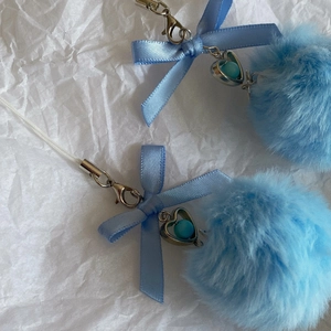 Detail of light blue fluffy pompom keychain with ribbon bow and silver heart charm