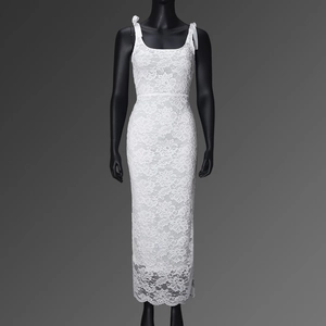 Detail of white lace maxi dress featuring bow shoulder straps and intricate floral textures
