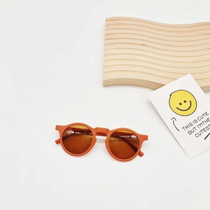 Detail shot of orange round frame kids sunglasses with dark lenses on a clean backdrop