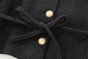 Detail of black tweed jacket with golden textured button and matching bow belt accent