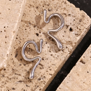Macro shot of silver liquid metal streamline earrings on textured beige stone base