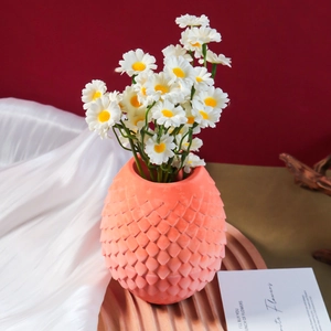 Detail of salmon-colored scale textured vase with faux daisies on a wavy wood base