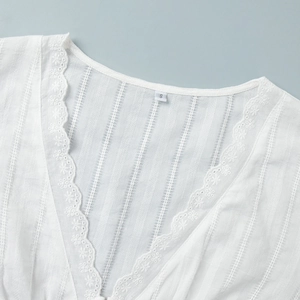 Detailed view of white V-neck blouse with lace trim and vertical striped fabric texture