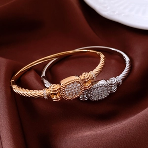 Nahaufnahme von gedrehten 18K Gold- und Silberarmbändern mit Kristallpavé auf Seidenstoff