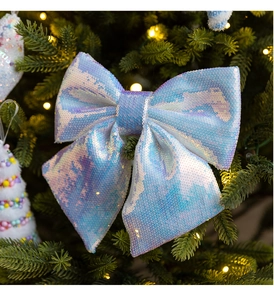 Close-up of iridescent sequin bow ornament hanging on a glowing Christmas tree branch