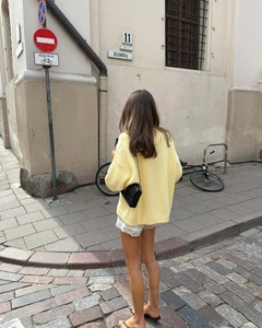 Outdoor street view of the back of a loose pale yellow knitted sweater with letter print