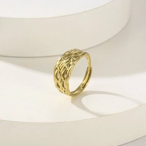 Detailed view of golden woven mesh adjustable open ring on a white geometric stand