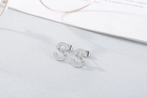 Detail of silver S-shaped stud earrings with Smile engraving on textured grey background