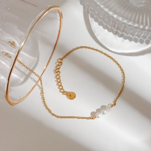 Minimalist gold stainless steel anklet featuring three white freshwater pearls on white background