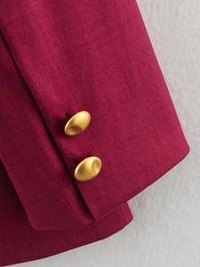 Close-up of burgundy blazer sleeve with dual matte gold buttons and woven texture