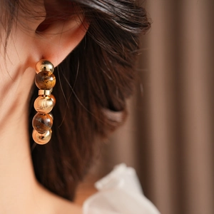 Detalle de pendientes vintage en forma de C con cuentas de ojo de tigre y esferas doradas