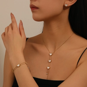 Detail of 18k gold plated stainless steel jewelry set with white heart pendants on a model