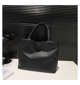 Detail of a large black woven leather tote bag on a white desk with modern office decor
