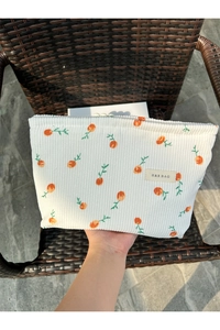 Handheld view of corduroy makeup bag with orange fruit pattern and brand label