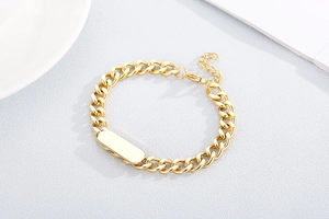 Detail of a gold Cuban chain bracelet with a blank rectangular plaque on white texture