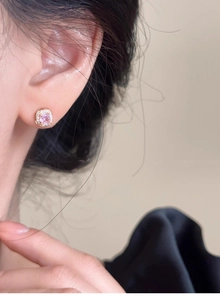 Close-up of a square pink gemstone earring with gold base and diamond halo on model