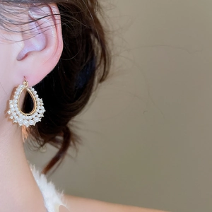 Detail of elegant gold pearl drop earrings worn by a model in warm studio lighting