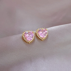 Macro shot of pink heart-shaped earrings with a sparkling diamond halo on silk