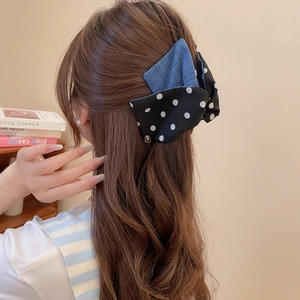Detailed view of large denim and polka dot bow hair clip worn on long brown hair