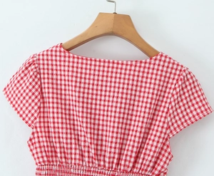 Detail of red and white plaid top with smocked waist hanging on a wooden hanger