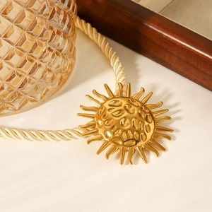 Detail of golden sun pendant with hammered texture and woven rope chain design