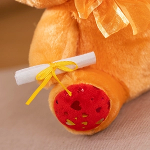 Close-up of plush bear paws with red sequin hearts and a white graduation scroll detail